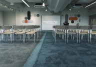Empty conference room set up with rows of chairs facing a projector screen displaying 