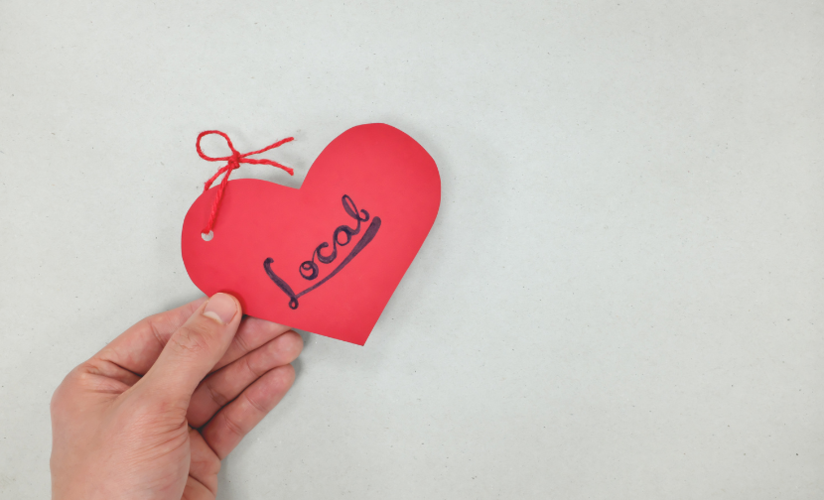 A hand holding a red heart-shaped tag with the word 