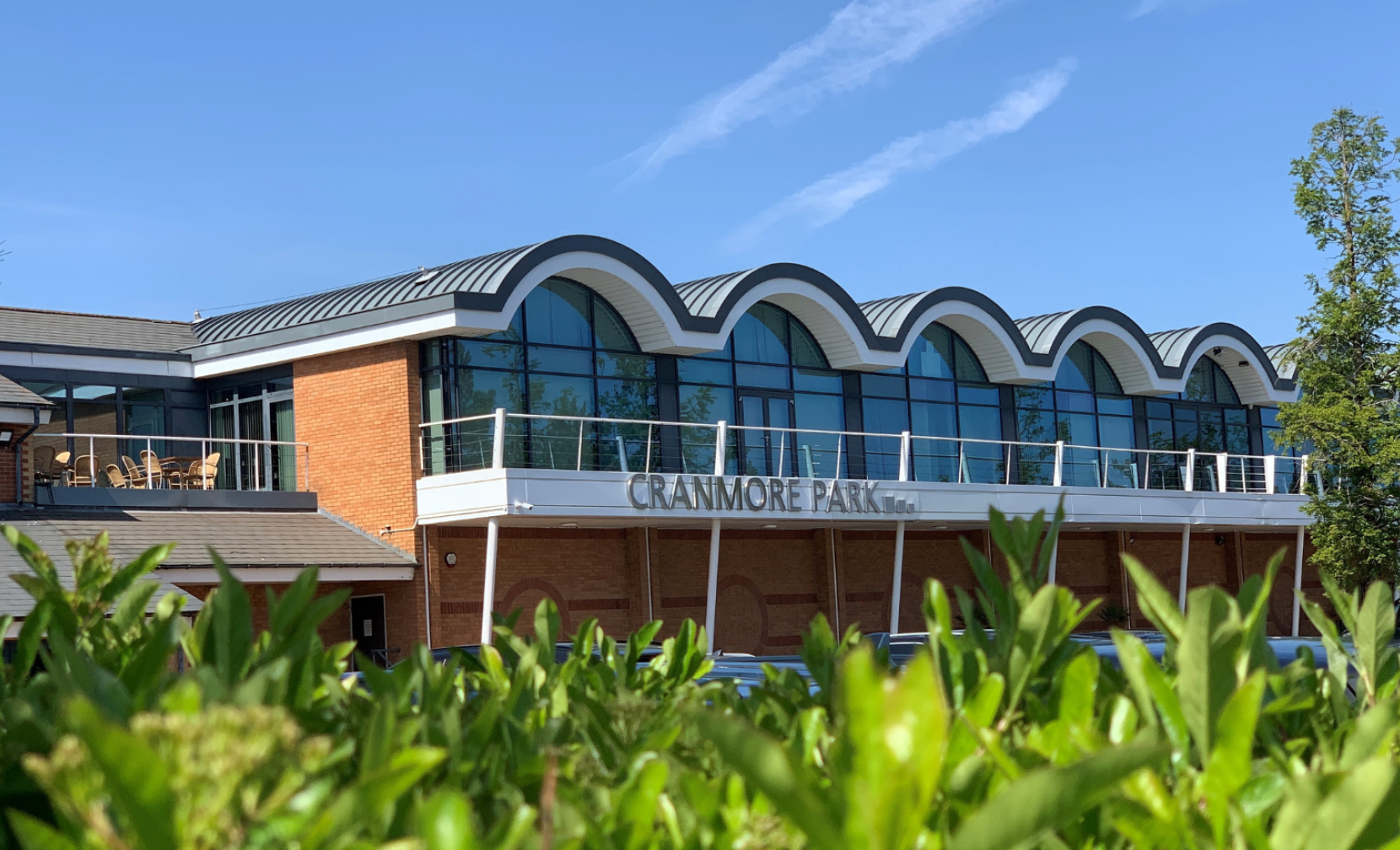 A modern building with large arched windows and a gray roof showcases the name 