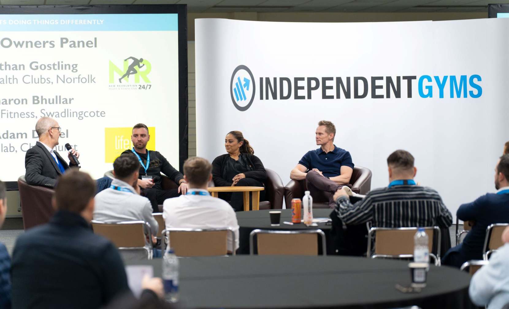 A panel discussion featuring four speakers seated on stage, with a large 