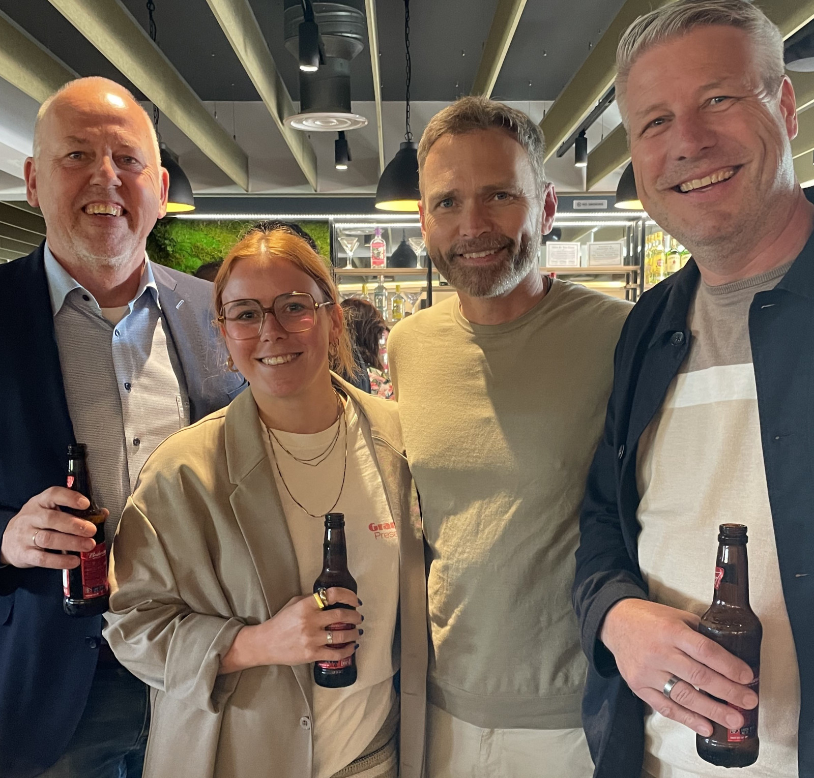 four people with beers in hand, smiling at the camera