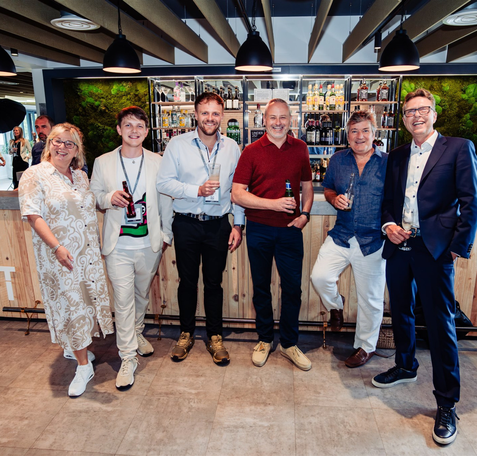 a group of six people standing in front of a bar, smiling at the camera