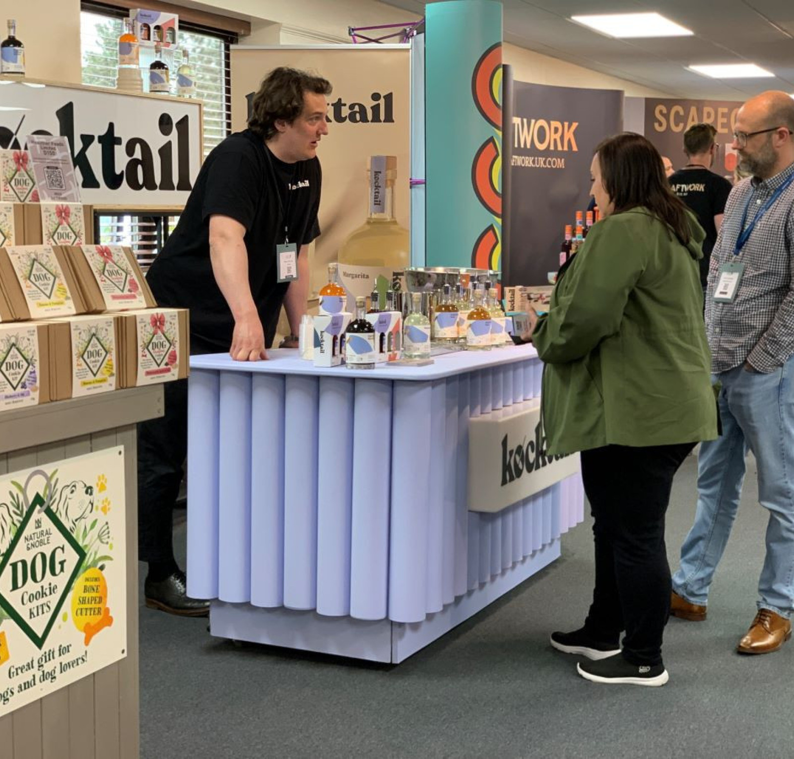 A vendor at a trade show is demonstrating products at a booth labeled 