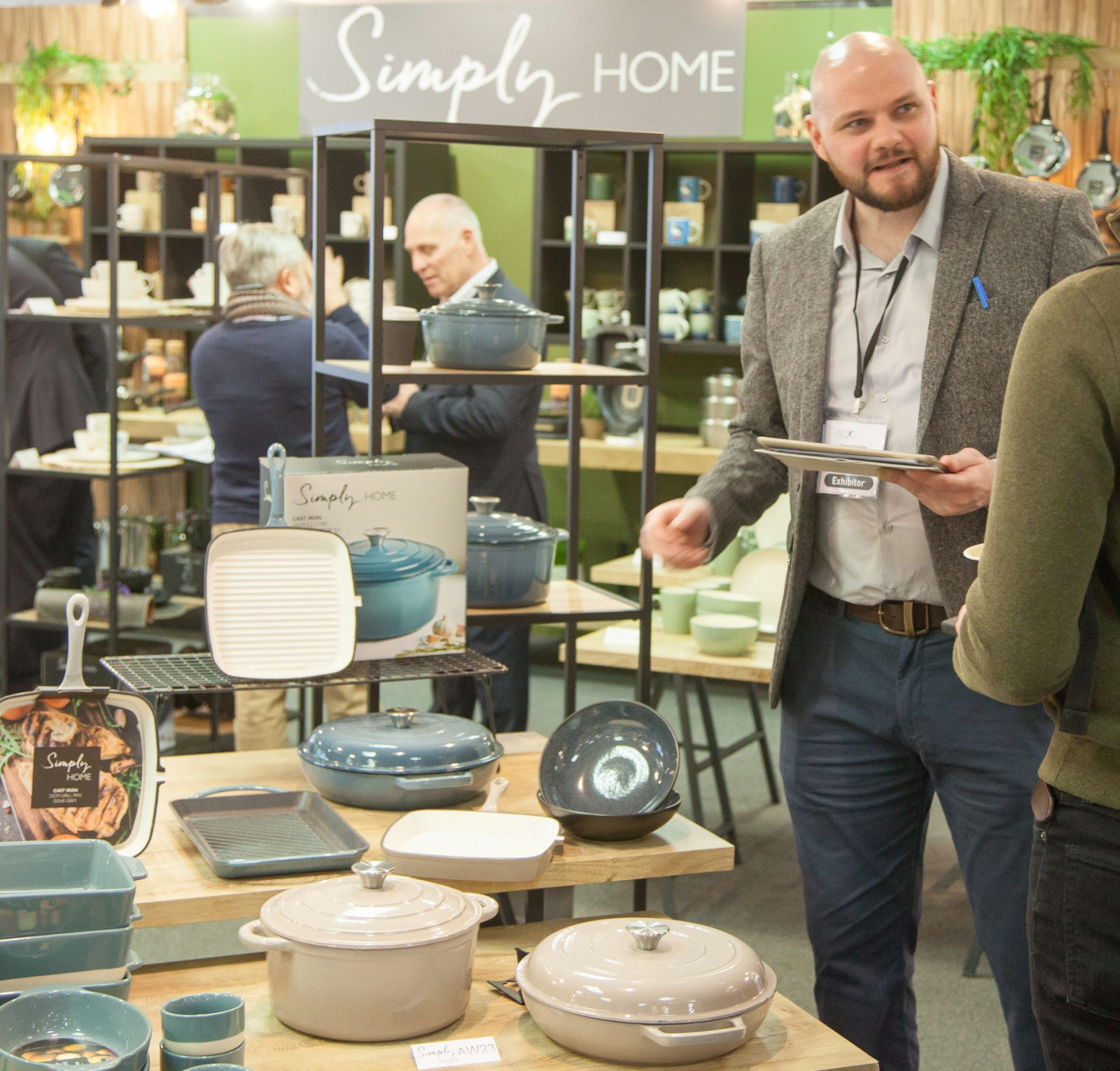 A vendor discusses kitchenware with a customer at a trade show, surrounded by various colorful cookware displayed on tables.