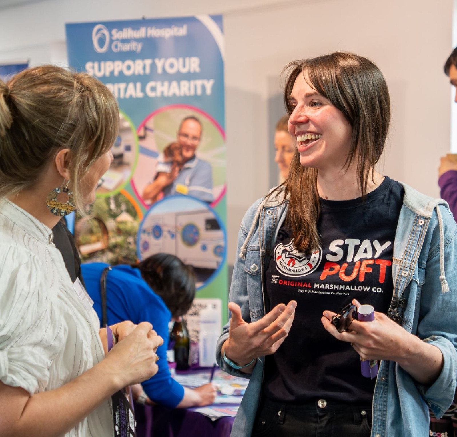 Two women are engaged in a conversation at a charity event. One woman, wearing a 