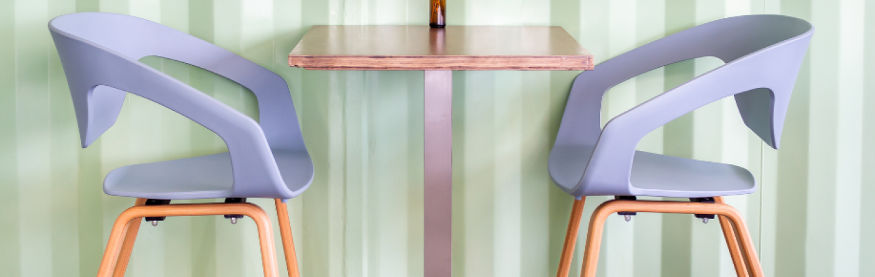 Two modern chairs with curved backs are positioned around a small wooden table against a green striped wall. The chairs have wooden legs and are designed for comfort.