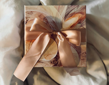 A beautifully wrapped gift box with a colorful, abstract design and a large satin bow sits on a white cloth surface.