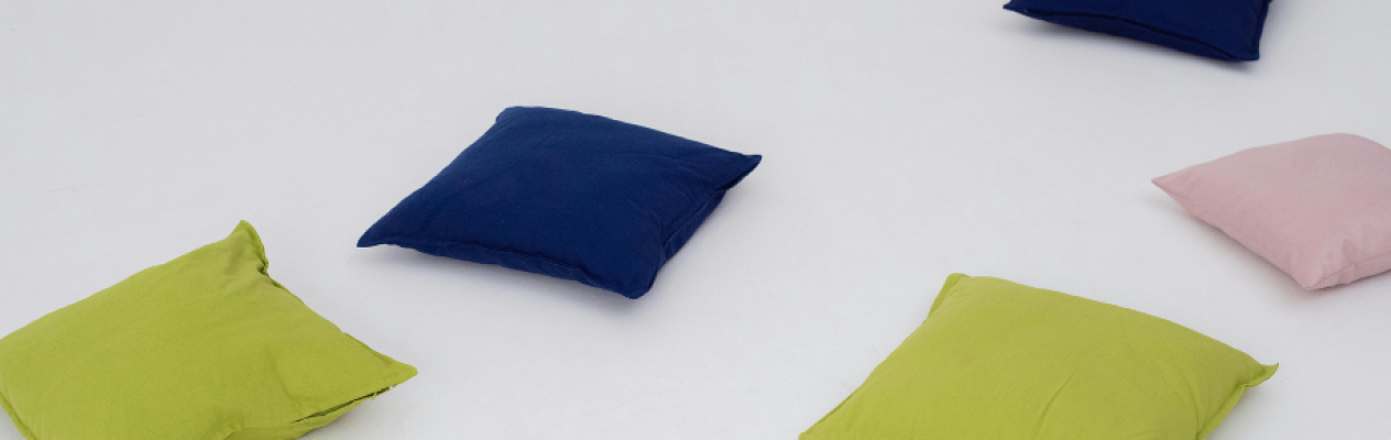 A scattered arrangement of soft, square cushions in navy blue, lime green, and light pink on a white background.