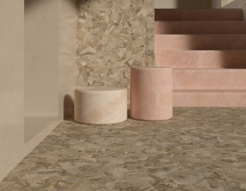 A minimalist interior scene featuring two cylindrical stone stools in soft hues of pink and beige. The background showcases a textured wall and a staircase, all with a warm, earthy color palette. The floor is covered in a patterned surface that complements the overall aesthetic.