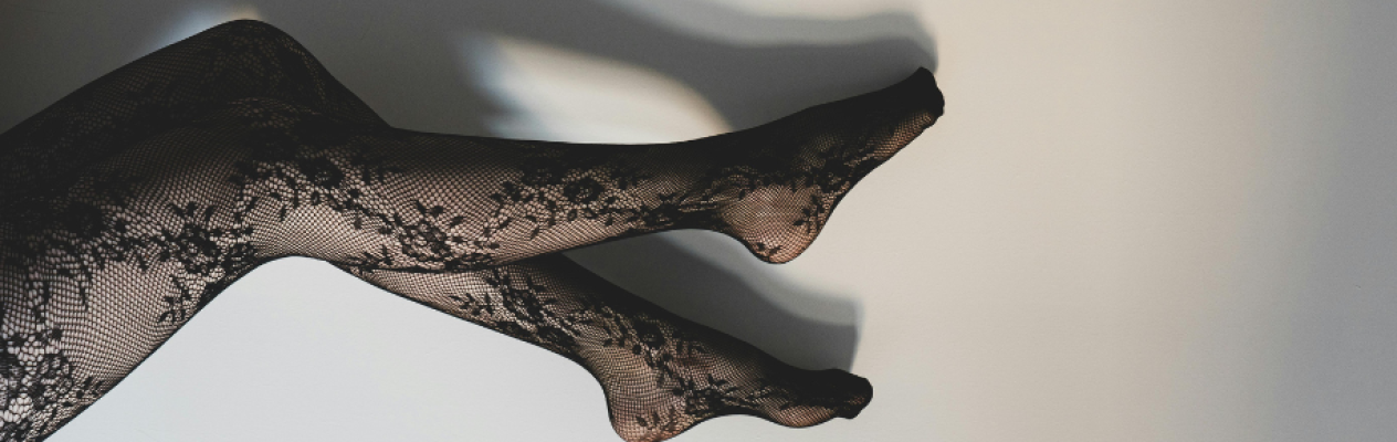 Black lace tights draped elegantly against a light background. The design features intricate patterns, showcasing the legs in a relaxed position. Shadows softly contrast the details of the tights.