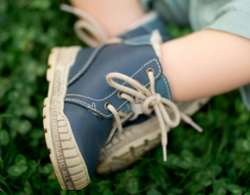 A close-up of a child's foot wearing navy blue lace-up boots, resting on a bed of green grass.