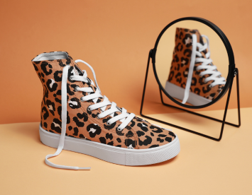 Leopard print high-top sneaker with white laces displayed next to a round mirror on an orange background.