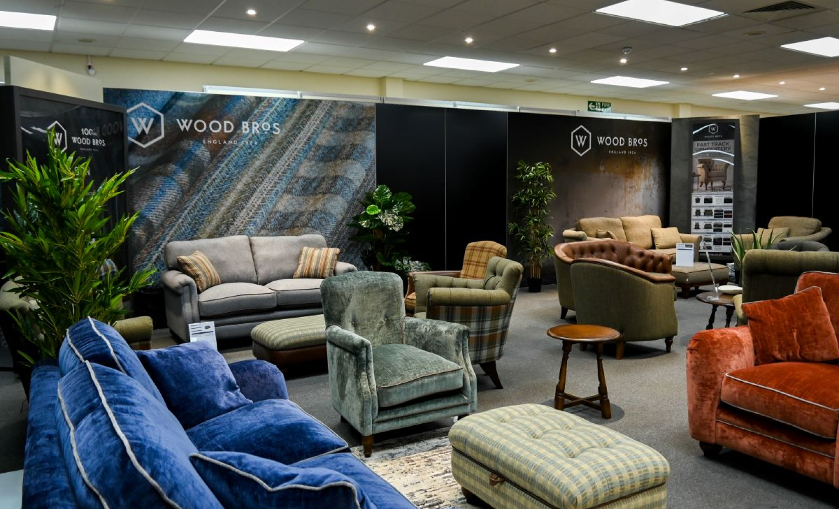A well-decorated furniture showroom featuring various upholstered sofas and armchairs in different styles and colors. The backdrop displays branding for 