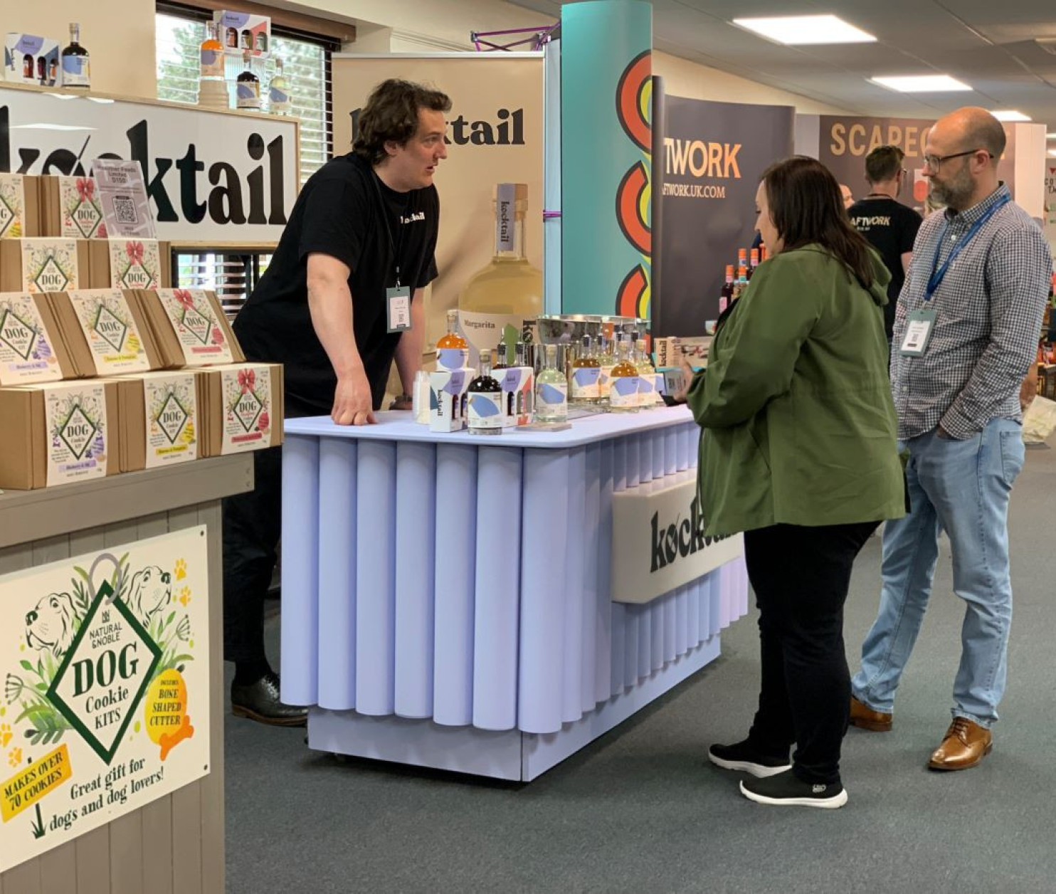 A vendor at a trade show is demonstrating products at a booth labeled 