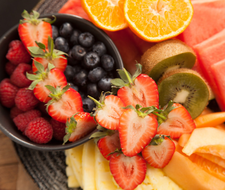A colorful fruit platter featuring watermelon slices, orange segments, kiwi, cantaloupe, pineapple, blueberries, raspberries, and fresh strawberries.