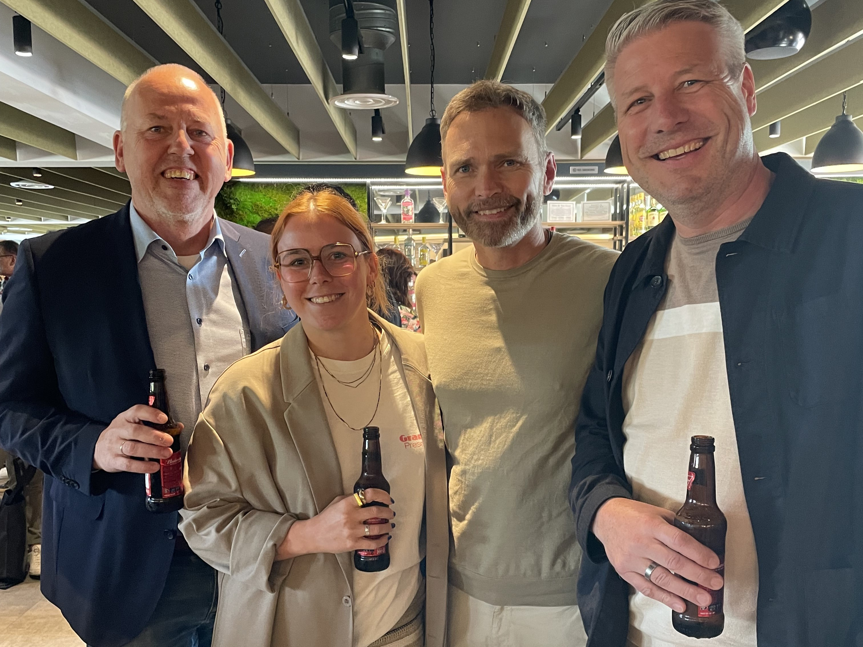 four people with beers in hand, smiling at the camera