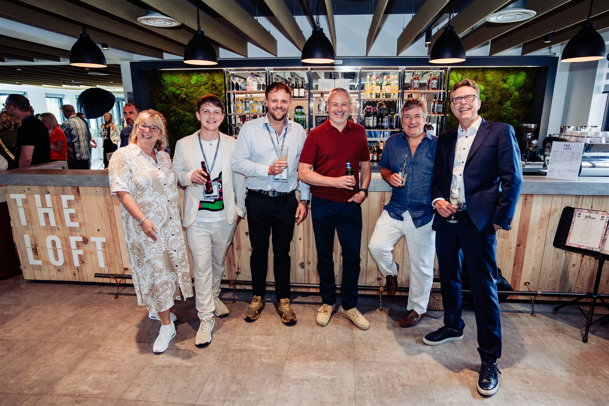 a group of six people standing in front of a bar, smiling at the camera