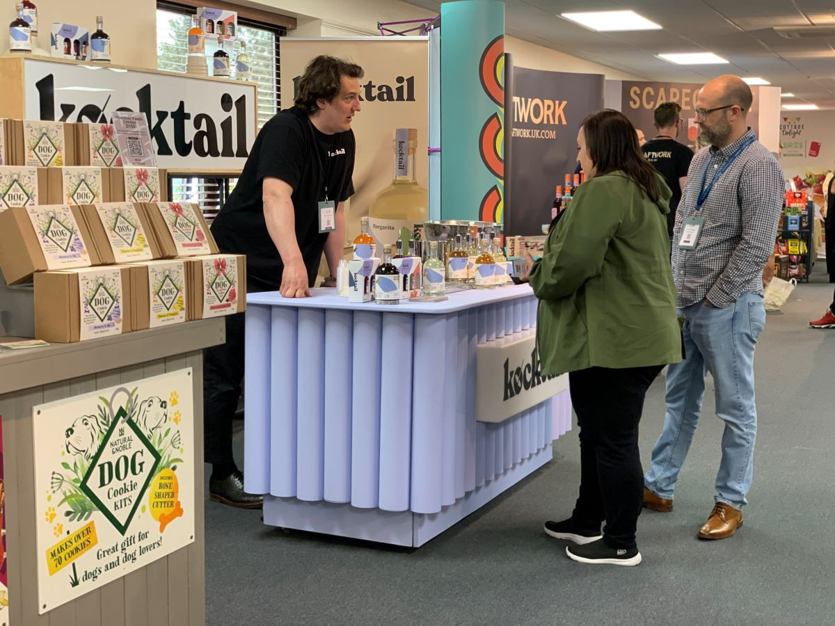 A vendor at a trade show is demonstrating products at a booth labeled 