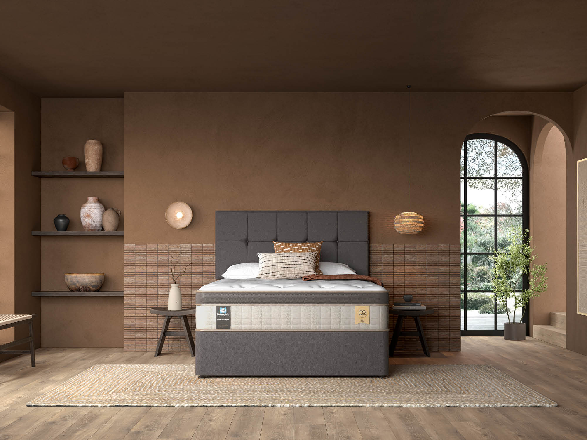 A stylish bedroom featuring a modern bed with a gray upholstered headboard. The bed is dressed in neutral bedding, complemented by decorative pillows. Surrounding the room are earthy tones, with shelves displaying vases and art pieces. A large window lets in natural light, revealing greenery outside. A woven rug adds texture to the wooden floor.